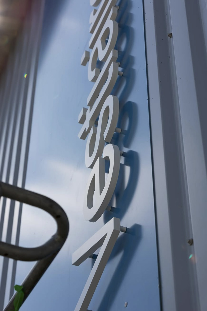 Gros plan sur une lettre découpée noire fixée sur façade en pierre avec jeu d'ombre, réalisation d'enseigne à Pau par Griffe Communication